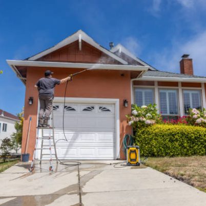 High quality stock photo of a middle aged man power washing a single-family home.